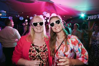 Twee gasten in kleurige outfits en hartvormige zonnebrillen dansen vrolijk op het trouwfeest van Liëla en Jeffrey in Paviljoe