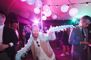Bruidegom Jeffrey met veren boa op feestelijk trouwfeest, roze verlichte danszaal met lampionnen in Paviljoen Twiske - Trouws