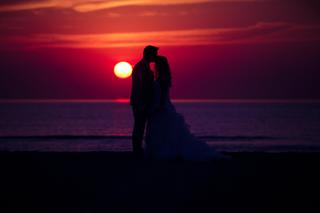 Ferry en Sabine kussen bij zonsondergang op strand Wijk aan Zee, de zon gloeit achter hun silhouetten - Trouwshoot Stefan Seg