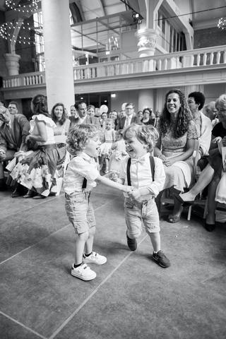 Twee bruidsjonkers dansen uitgelaten in Sint Nikolaaskerk terwijl gasten toekijken - Trouwshoot Stefan Segers