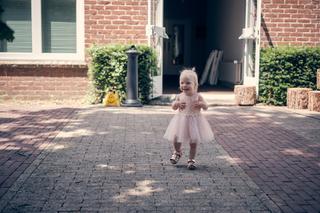 Blij peuter in roze jurkje rent over de kindvriendelijke binnenplaats van Fletcher hotel Deurne - Trouwshoot Stefan Segers
