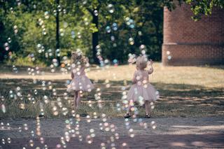 Twee blonde meisjes in roze jurkjes blazen zeepbellen in de zon op het terras - Trouwshoot Stefan Segers