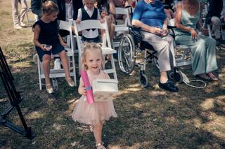 Kleine bruidsmeisje in roze tutu met felroze rol op grasveld omringd door gasten op stoelen - Trouwshoot Stefan Segers