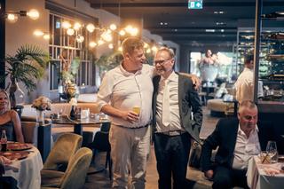 Twee gasten genieten lachend van elkaar tijdens het feest in de elegant verlichte zaal van Fletcher hotel Deurne - Trouwshoot