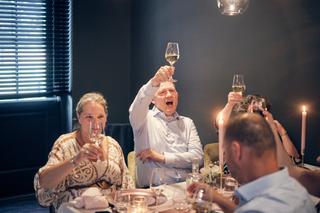 Man in wit overhemd heft glas omhoog voor een toast, vrouw lacht mee aan tafel met kaarsen - Trouwshoot Stefan Segers