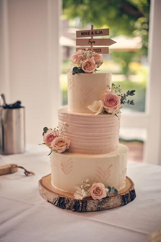 Elegante drielaagse bruidstaart met gestapelde lagen, roze rozen en houten naamtopper voor Mike en Ilja - Trouwshoot Stefan S