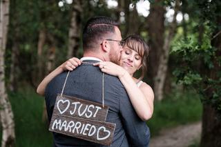 Bruidspaar Barry en Milou omhelzen elkaar met Just Married bord in bos - Trouwshoot Stefan Segers