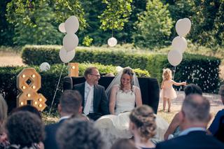 Bruidspaar Mike en Ilja zit samen op hun trouwdag in een vintage auto omgeven door witte ballonnen en gasten op Fletcher hote