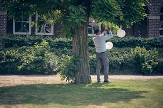 Bruidegom hangt lampionnen op in de groene tuin bij Fletcher hotel Deurne - Trouwshoot Stefan Segers