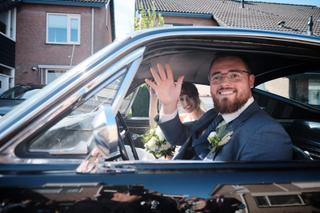 Bruidspaar Barry en Milou zwaaien vrolijk uit auto na ceremonie Bavokerk - Trouwshoot Stefan Segers
