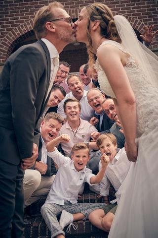 Bruidspaar Mike en Ilja kust elkaar omringd door vrolijke gasten bij Klein kasteel Deurne - Trouwshoot Stefan Segers