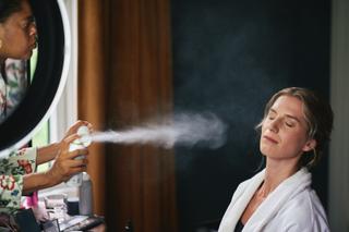 Bruid Karien krijgt make-up spray toegediend door vrouw tijdens trouwvoorbereiding - Trouwshoot Stefan Segers