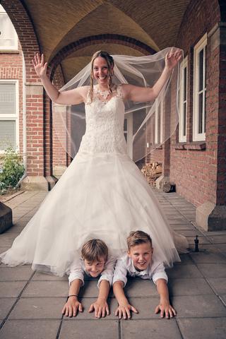 Bruid Ilja speels met bruidskinderen onder bakstenen boog op Fletcher Hotel Klein Kasteel Deurne - Trouwshoot Stefan Segers