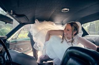 Bruid Ilja lacht voluit in vintage auto, kostuum om haar heen, moment vol blijdschap - Trouwshoot Stefan Segers