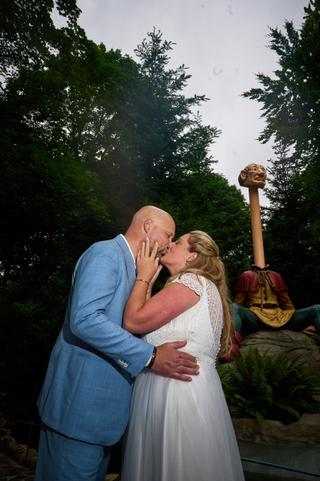 Annemarie en Jan kussen elkaar voor de kunstenaar in Efteling, omgeven door groen - Trouwshoot Stefan Segers