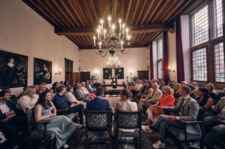 Simanca en Harm-Jan's huwelijksceremonie in historische zaal Huszár Delft, gasten luisteren aandachtig onder kristallen kroon