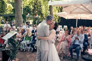 Bruidspaar Evelien en Krijn kussen tijdens ceremonie in tuin De Schaapskooi Delft, gasten applaudisseren, trouwreportage - Tr