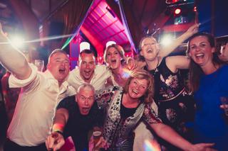 Bruidsgasten vieren feest op trouwreportage Ingrid en Clive in Delft, dansende groep onder roze discolicht - Trouwshoot Stefa