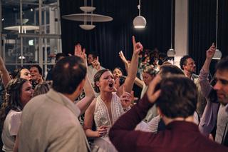 Simanca en Harm-Jan dansen vol energie met hun gasten op het feest in Delft. Handen omhoog, pure vreugde - Trouwshoot Stefan