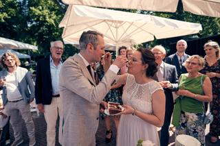 Bruidspaar Krijn en Evelien snijdt taart tijdens receptie onder parasols in De Schaapskooi Delft, trouwreportage - Trouwshoot