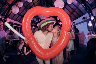 Bruidspaar Evelien en Krijn kussen in rood hartballonnen feestdecor, trouwfeest De Schaapskooi Delft, bruidsfotografie - Trou