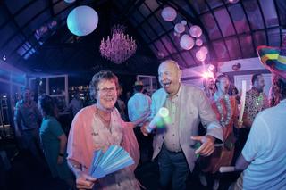 Bruidspaar Evelien en Krijn dansen feestelijk op receptie met gekleurde lichtjes, trouwreportage De Schaapskooi Delft - Trouw