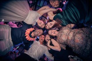 Bruidspaar Evelien en Krijn feest met gasten op trouwfeest De Schaapskooi Delft, dansende groep onder paars licht - Trouwshoo