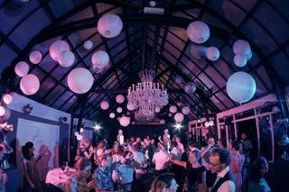 Bruidspaar Evelien en Krijn feesten met gasten in feestlocatie De Schaapskooi Delft, roze verlichting en kroonluchter, trouwr