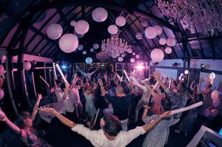 Bruidspaar Evelien en Krijn dansen met gasten in feestend interieur De Schaapskooi Delft, roze lampionnen en kroonluchter, tr