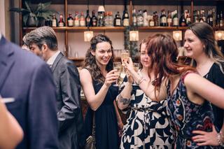 Bruidsgasten proosten met champagne in moderne bar Huszár Delft, vrolijke sfeer en glimlachende gezichten - Trouwshoot Stefan