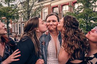 Simanca omringd door vriendinnen die haar op het terras kussen, puur geluk en verbondenheid in Delft - Trouwshoot Stefan Sege