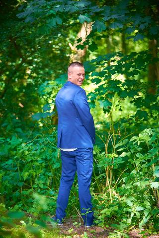 Bruidegom Jeffrey in blauw pak tussen groen bladerig bos, trouwreportage Delftse Hout Voorburg - Trouwshoot Stefan Segers