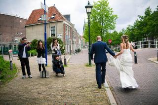 Bruidspaar Renate en Jesse loopt hand in hand door historische straat Delft, gasten fotograferen, trouwreportage - Trouwshoot