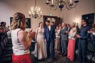 Bruidspaar Simanca en Harm-Jan wordt toegejuicht door gasten in de elegante zaal van Huszár in Delft, onder kristallen kroonl