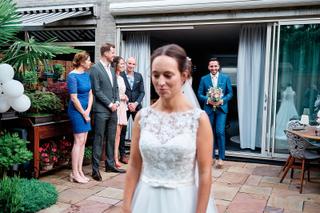 Bruid Tessa in kant jurk op terras, bruidegom Jeroen met bruidsboeket zichtbaar, huwelijksreportage Het Rieten Dak Delft - Tr