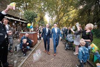 Bruidspaar Mathijs en Jeroen loopt hand in hand door Delftse Hout, bubbels zweven rond, gasten juichen, trouwreportage - Trou