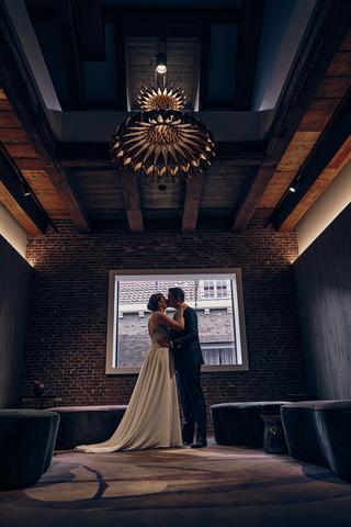 Bruidspaar Harm-Jan en Simanca kussen onder industriële kroonluchter in Hotel Arsenaal Delft - Trouwshoot Stefan Segers