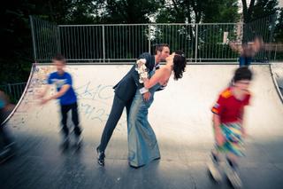 Bruidegom tilt bruid op in skatebowl met speelse kinderen op achtergrond - Trouwshoot Stefan Segers