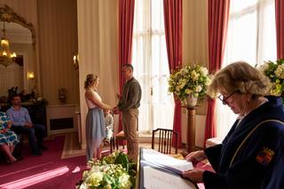 Elise en Erik wisselen trouwgeloften in een elegant interieur met rode gordijnen. Een intiem moment onder toezicht van de amb