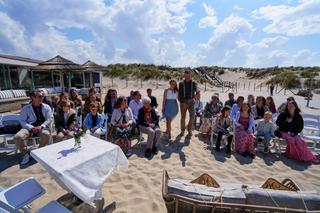 Elise en Erik trouwen op het strand bij Beachclub Titus in Kijkduin. Gasten op het zand onder blauwe lucht - Trouwshoot Stefa