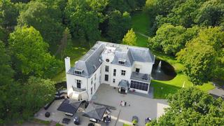 Luchtfoto van landgoed Te Werve met het elegante witte herenhuis omgeven door weelderig groen, gasten op het terras tijdens d