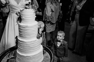 Kleine bruidsjongertje in pak bewondert de bruidstaart tussen de gasten op het feest van Karlijn en Glenn - Trouwshoot Stefan