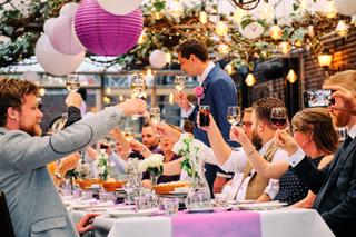 Bruidspaar Manon en Alvin toasten met gasten onder paarse lampionnen, trouwreceptie Prinsenhof Delft - Trouwshoot Stefan Sege