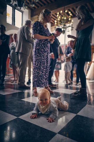 Kleine Hudson kruipt lachend over de dansvloer terwijl gasten toekijken op de bruiloft van Yvo en Marjolein - Trouwshoot Stef