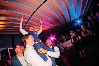 Bruidegom Stefan geheven door gasten tijdens feestelijke trouwreceptie Waterreus, dynamische bruidsfotografie - Trouwshoot St