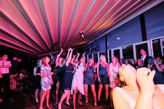 Bruidspaar Stefan en Victoria boeketten gooien op trouwfeest Waterreus, gasten vangen bloemen onder roze neonverlichting, fes