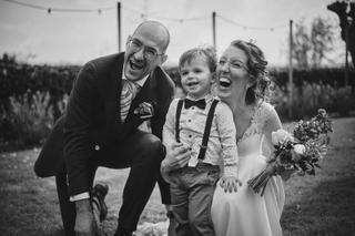 Bruidspaar Ilse en Robbert met kind lachend in veld bij Boerderij Burgersdijk De Lier, vrolijke trouwfoto - Trouwshoot Stefan