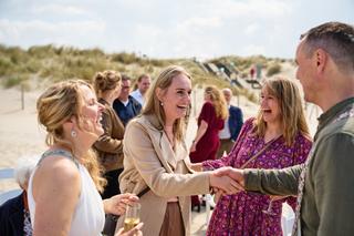 Tijdens de bruiloft van Elise en Erik bij Beachclub Titus in Kijkduin: bruid lachend met gasten op het strand - Trouwshoot St