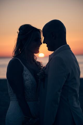 Bruidspaar Chris en Gerco kijken elkaar aan bij zonsondergang op het strand, romantische trouwreportage Strandclub Naturel Sc