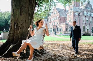 Bruid Mirjam op schommel bij eeuwenoude boom, bruidegom Nick kijkt toe, trouwreportage Duin & Kruidberg Bloemendaal - Trouwsh